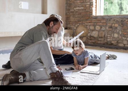 Mature man and woman reading documents with daughter lying on rug at home Stock Photo