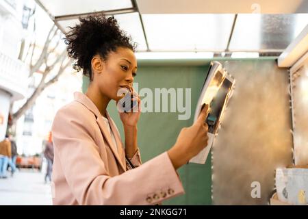 Businesswoman reading magazine and talking on smart phone Stock Photo