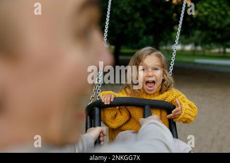 Father pushing daughter on swing at park Stock Photo