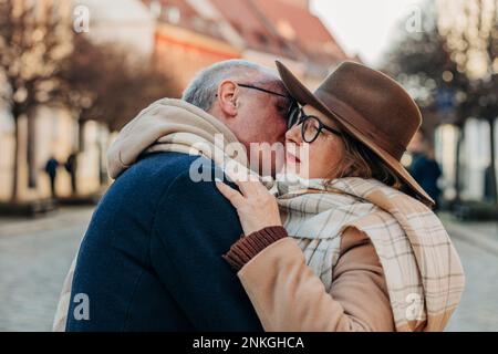 Senior man kissing woman wearing hat and scarf Stock Photo