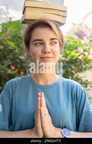 Smiling woman with hands clasped balancing books on head Stock Photo