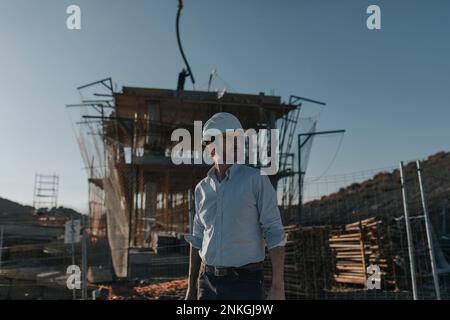 Contemplative architect wearing hardhat standing at construction site Stock Photo