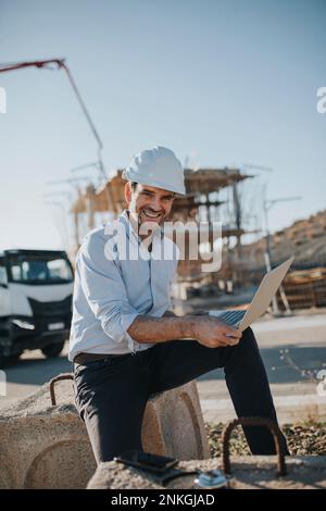 Happy mature architect with laptop at construction site Stock Photo