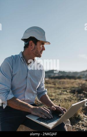 Thoughtful mature architect sitting with laptop in construction area Stock Photo