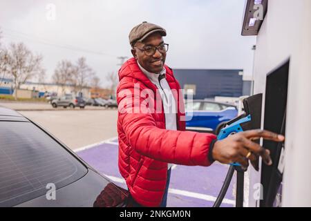 Smiling mature man using electric charging at station Stock Photo