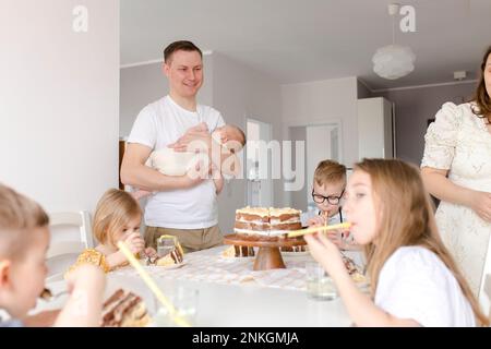 Father carrying son with children eating cake sitting at table Stock Photo
