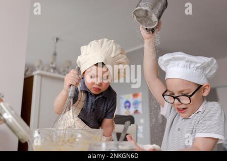 Boy sieving flour by brother mixing batter with whisk in kitchen Stock Photo