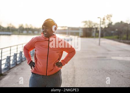 Smiling woman with wireless headphones exercising at promenade Stock Photo