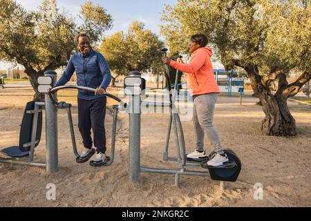 Happy senior couple exercising at outdoor equipment at park Stock Photo