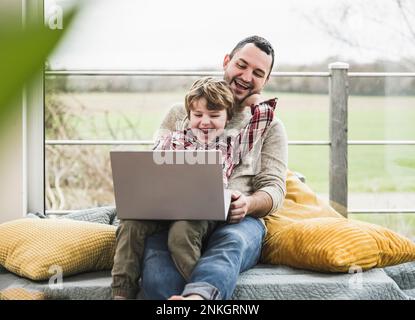 Happy father and son using laptop together in front of window at home Stock Photo