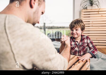 Smiling son with father doing arm wrestling at home Stock Photo