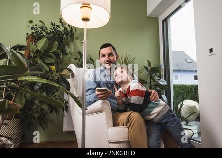 Son with father controlling light of floor lamp through smart phone Stock Photo