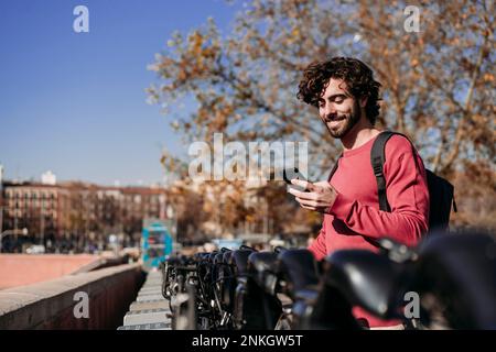 Happy man using mobile app to rent electric push scooter on sunny day Stock Photo