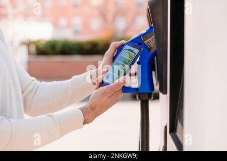 Man using electric car charging app on smart phone at station Stock Photo