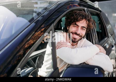 Happy young man leaning on car window Stock Photo
