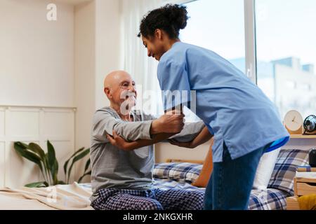 Nurse helping senior man to sit on bed at home Stock Photo