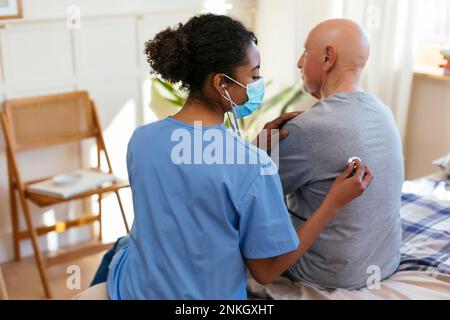 Nurse listening to senior patient's heartbeat using stethoscope at home Stock Photo