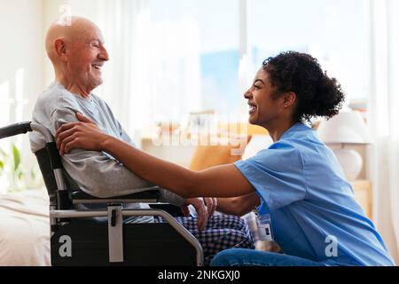 Happy physiotherapist talking to senior man sitting on wheelchair Stock Photo