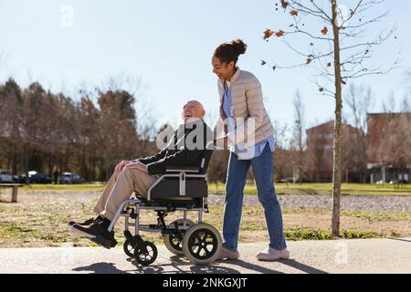 Woman assisting senior man on wheelchair in park Stock Photo