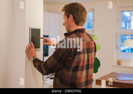 Man using smart home device on wall at home Stock Photo