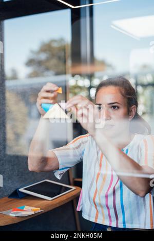 Young businesswoman sticking adhesive notes on glass Stock Photo