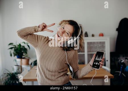 Carefree woman wearing headphones enjoying music and dancing at home Stock Photo