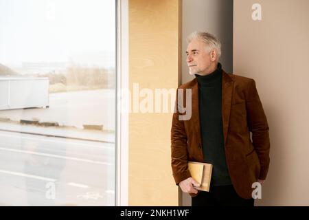 Smiling mature businessman looking through window Stock Photo