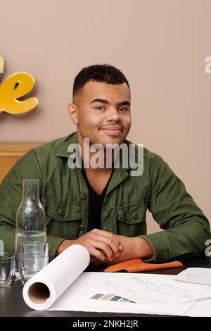 Smiling young fashion designer with sketch on desk at studio Stock Photo
