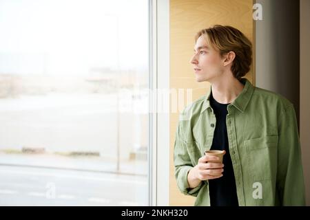 Thoughtful man looking out of window holding coffee cup Stock Photo