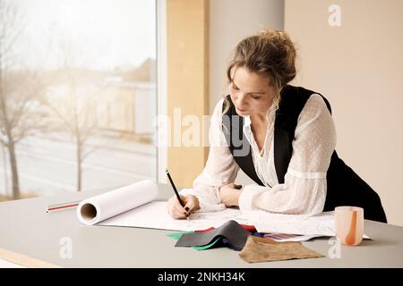 Mature fashion designer sketching on paper in studio Stock Photo
