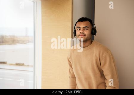 Smiling young man wearing headphones standing by window Stock Photo