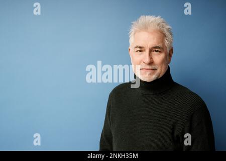 Smiling mature man wearing black turtleneck against blue background Stock Photo