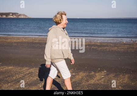 Smiling elderly woman walking by sea at beach Stock Photo