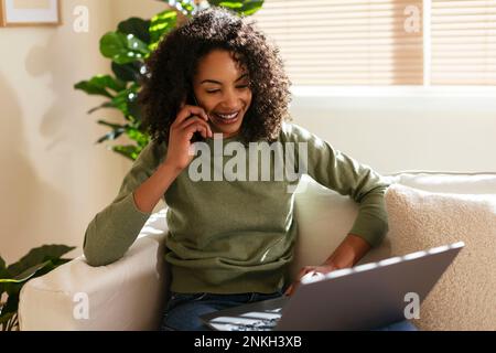 Smiling freelancer talking on mobile phone with laptop at home Stock Photo