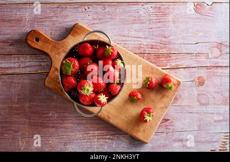 Colander with fresh strawberries lying on cutting board Stock Photo