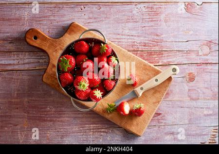 Colander with fresh strawberries lying on cutting board Stock Photo