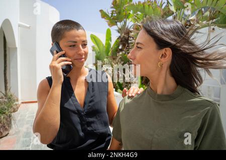 Smiling woman talking on smart phone looking at friend Stock Photo