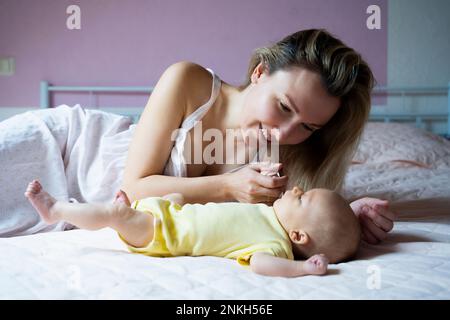 Smiling mother playing with baby boy lying on bed at home Stock Photo