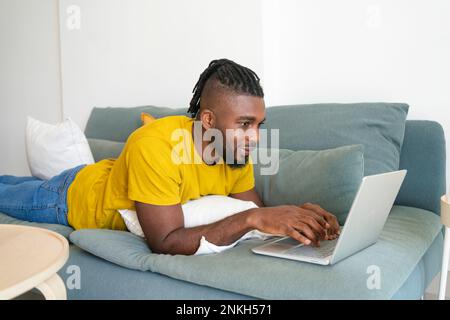 Freelancer lying on sofa and using laptop at home Stock Photo