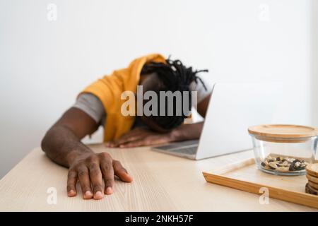 Tired freelancer leaning on desk with laptop Stock Photo