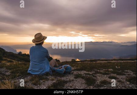 Mature Woman Wearing Hat While Sitting On Car During Sunset Stock Photo mature-woman-wearing-hat-while-sitting-on-car-during-sunset-stock-photo
