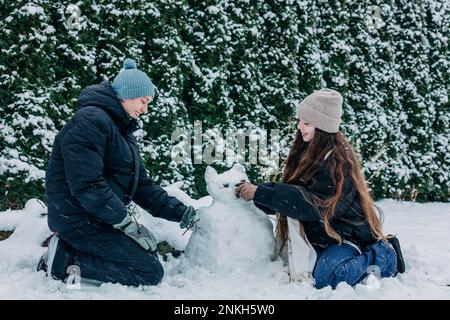 Smiling friends making snowman in winter at park Stock Photo