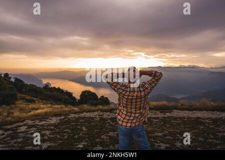 Mature man with hands behind head standing on mountain Stock Photo