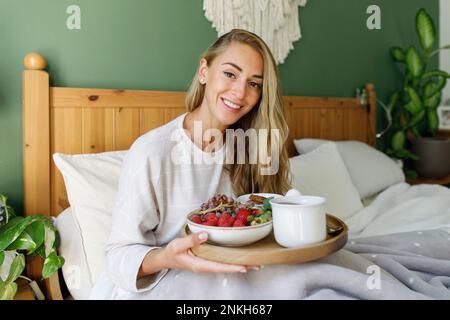 Happy woman holding breakfast in wooden tray on bed at home Stock Photo