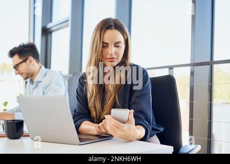 Businesswoman using smart phone by laptop at workplace Stock Photo