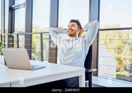 Relaxed businessman with hands behind head sitting on chair at office Stock Photo