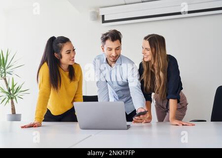 Smiling businessman using smart phone amidst colleagues at workplace Stock Photo