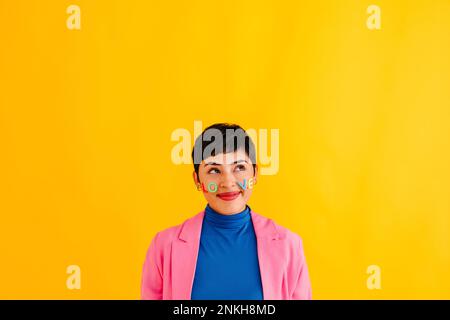 Thoughtful young woman with Love text stickers on face against yellow background Stock Photo