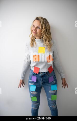 Thoughtful woman with colorful adhesive notes on body near wall Stock Photo