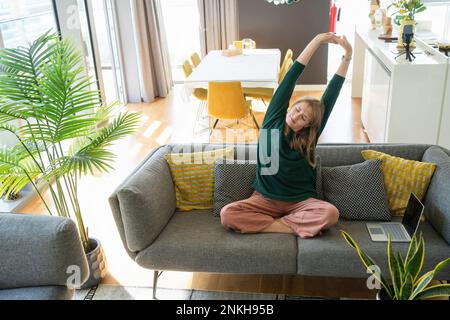 Woman stretching arms on sofa at home Stock Photo